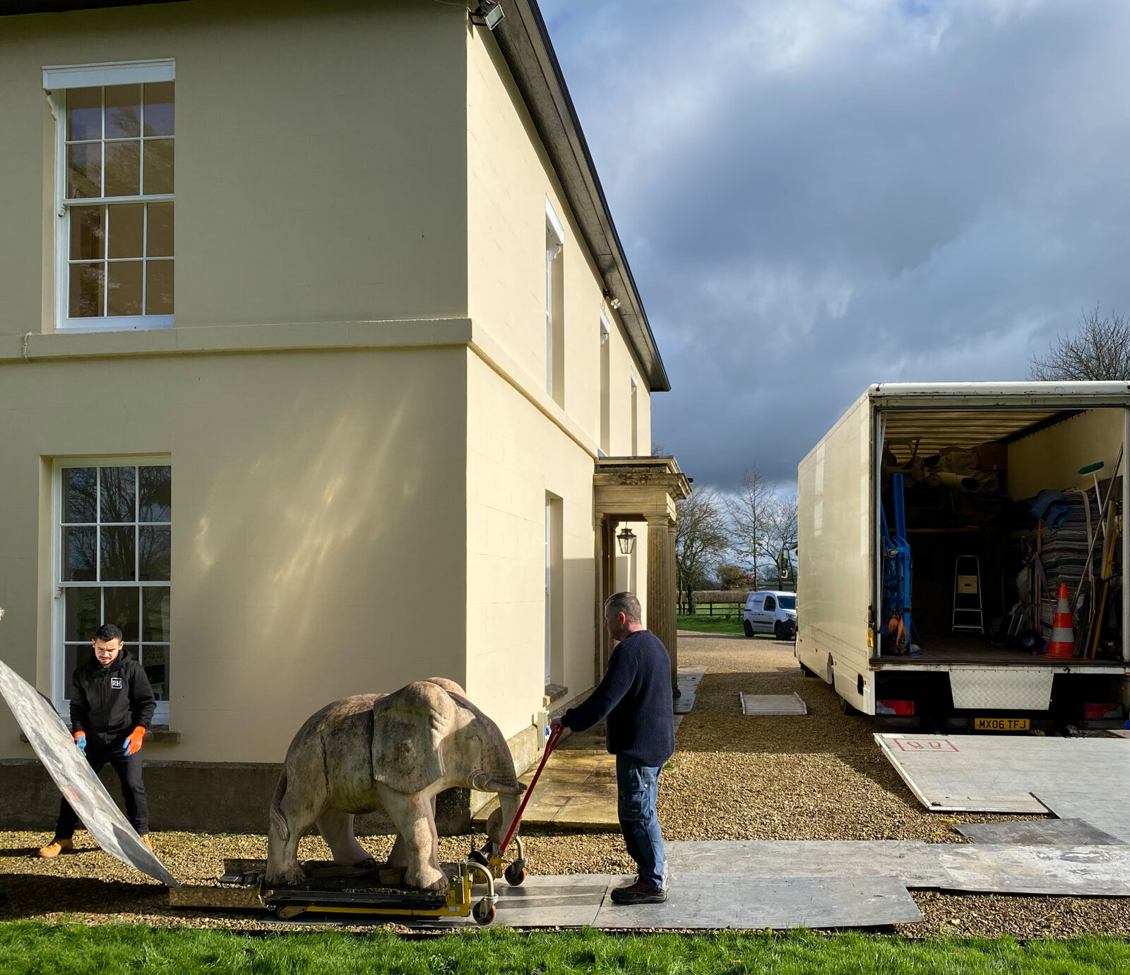 RH team moving a stone elephant statue on a trolley across protective boards outside a country house