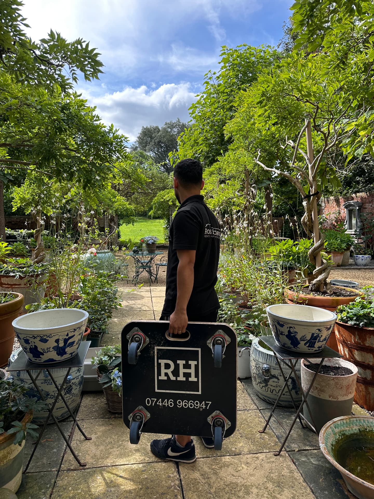 RH team member carrying a branded moving dolly through a walled garden